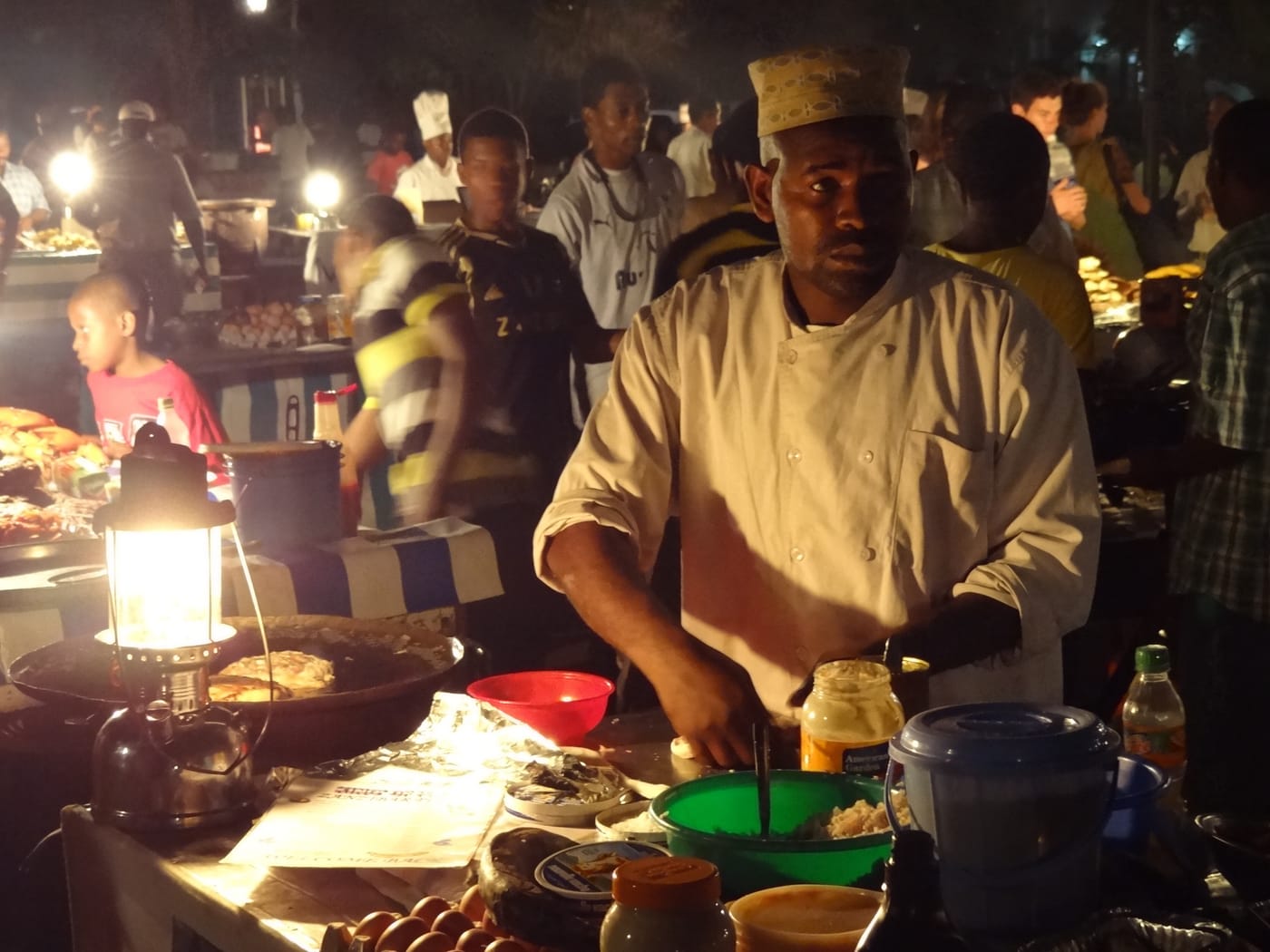 A vendor grilling seafood by lamplight at Forodhani night market